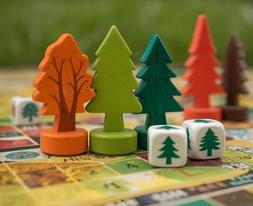 Mehrfarbige Spielfiguren in Baumform und Würfel mit Baum-Symbol auf einem Spielbrett